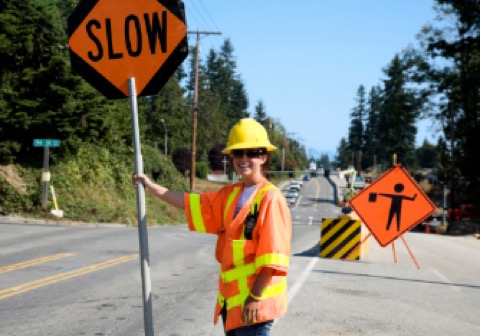 A flagger in high-visibility gear holding a SLOW paddle at the roadside.